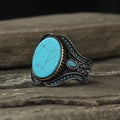 Men's antique silver alloy ring with a round band and a turquoise blue centrepiece on a hand.