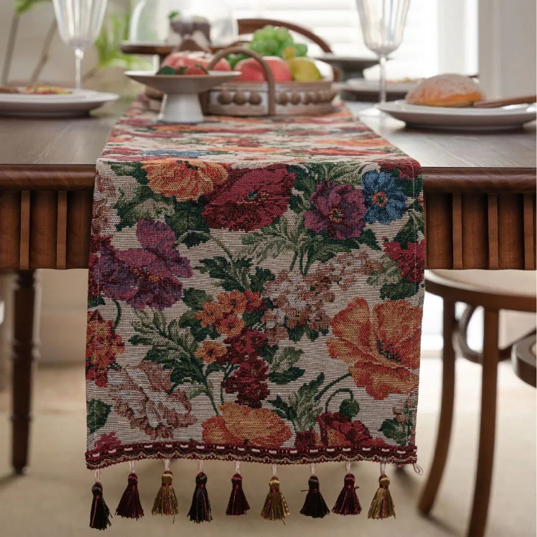 Long beige table runner with floral Jacquard pattern and tassels, shown on a wooden table.