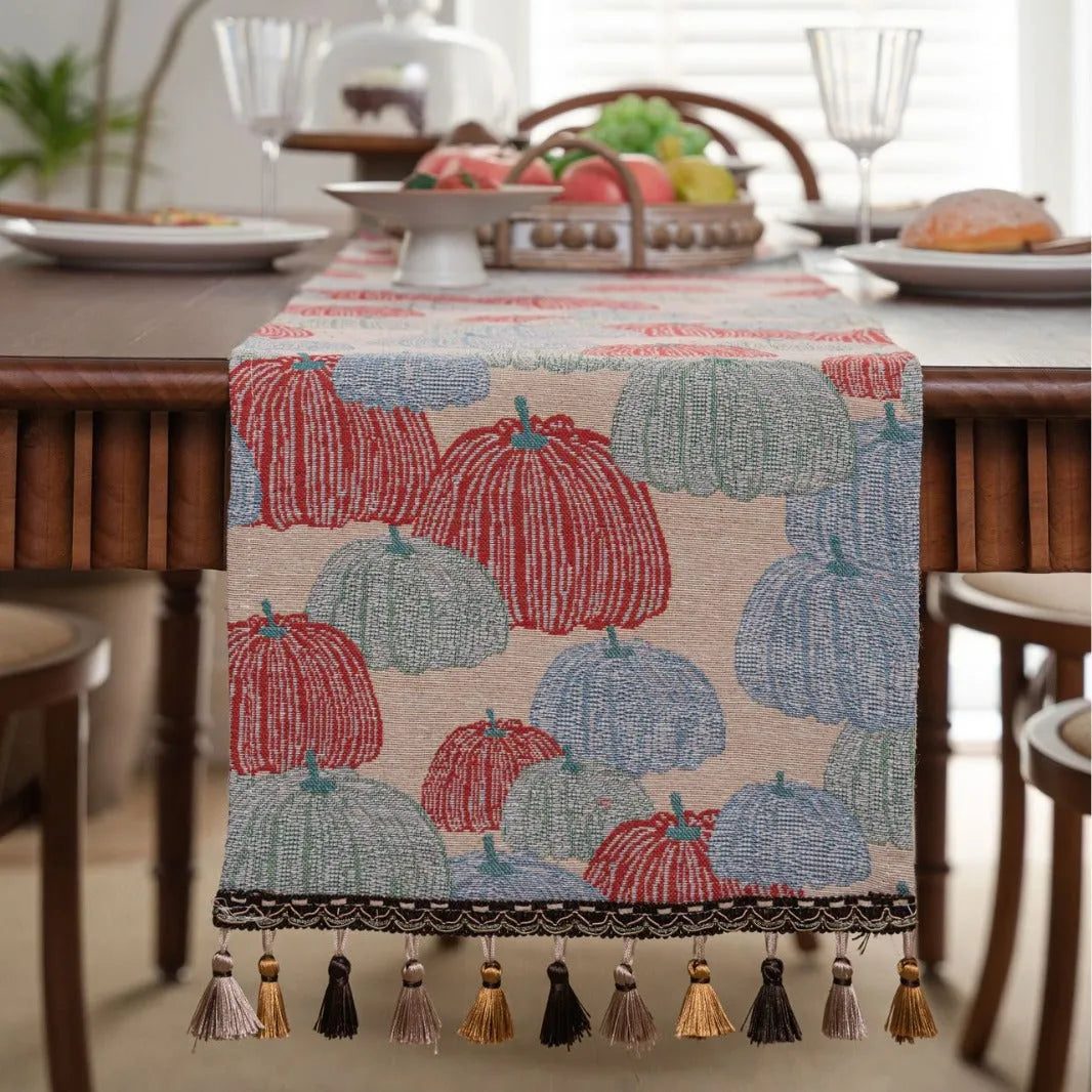 Long beige table runner with floral Jacquard pattern and tassels, shown on a wooden table.