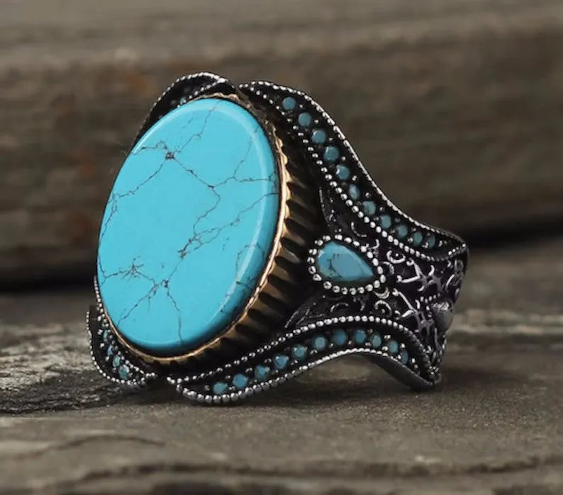 Men's antique silver alloy ring with a round band and a turquoise blue centrepiece on a hand.