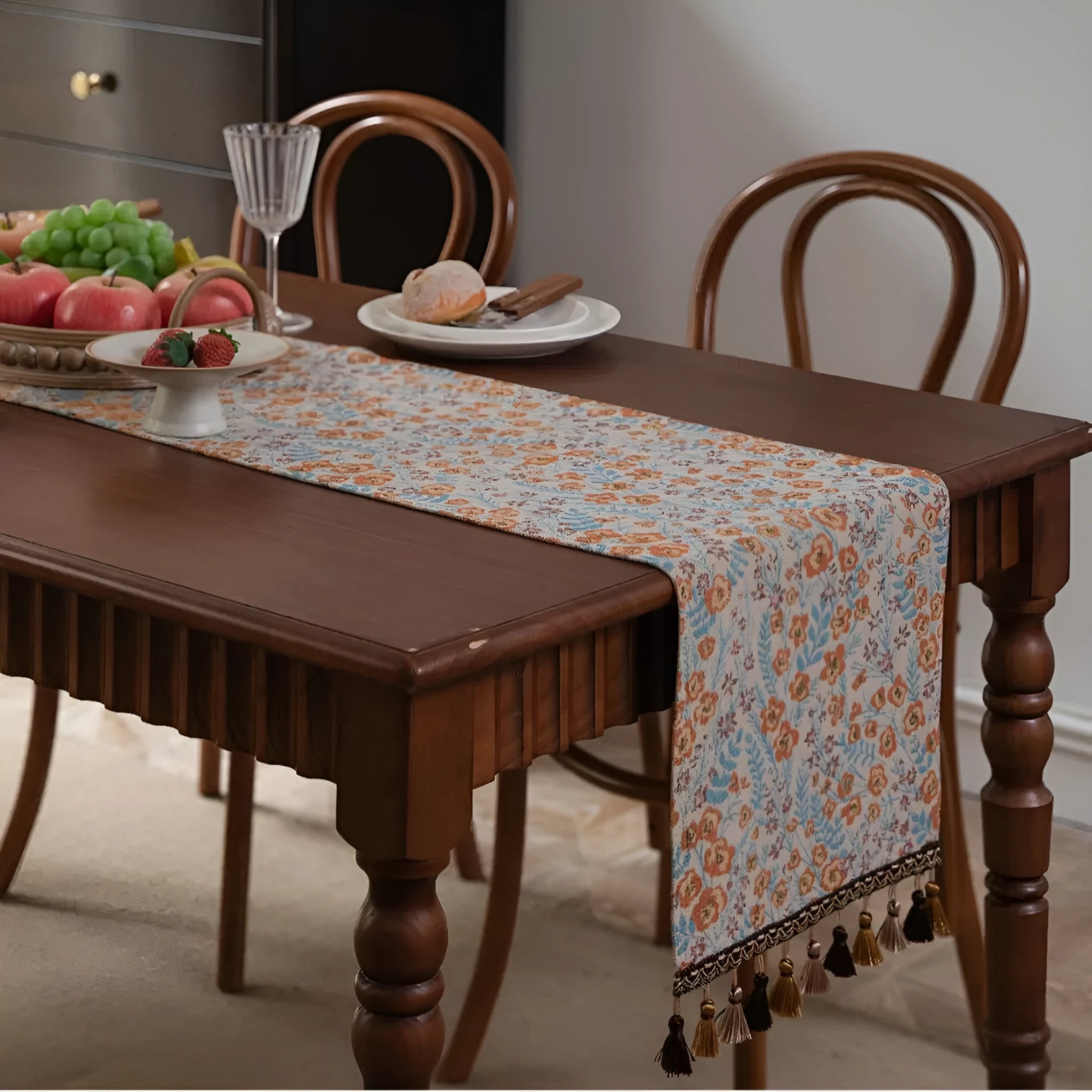 Long beige table runner with floral Jacquard pattern and tassels, shown on a wooden table.