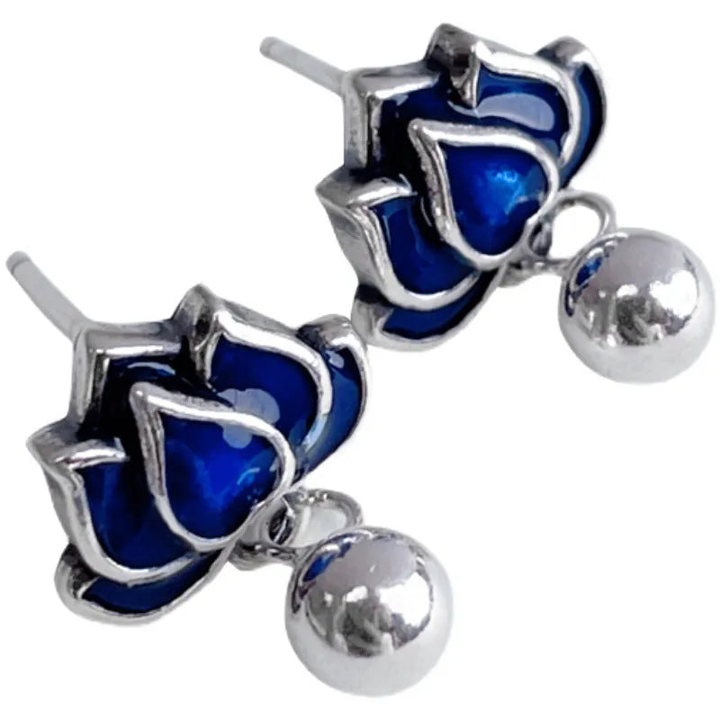 Close-up of blue lotus seedpod and tassel drop earrings in silver tone alloy on a white background.
