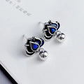 Close-up of blue lotus seedpod and tassel drop earrings in silver tone alloy on a white background.