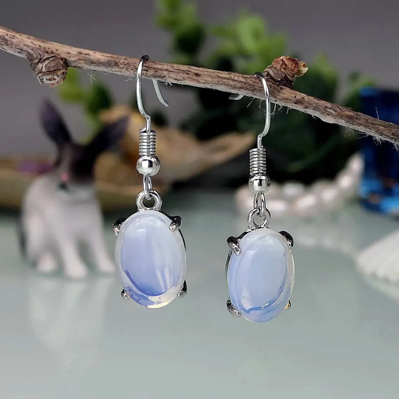 A pair of retro-style opal drop earrings in moonlight white with a cross detail and ellipse shapes.