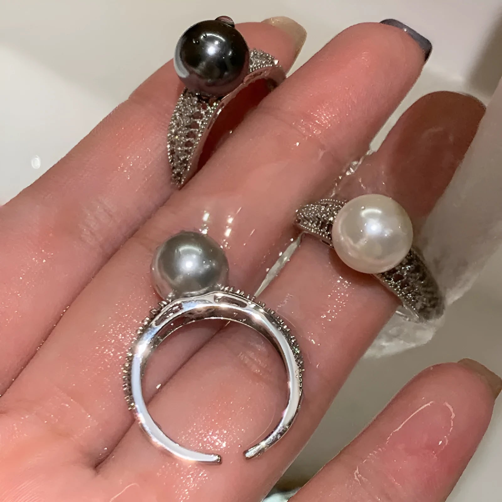 Geometric adjustable open ring in black pearl colour on a copper band, shown on a woman's index finger.