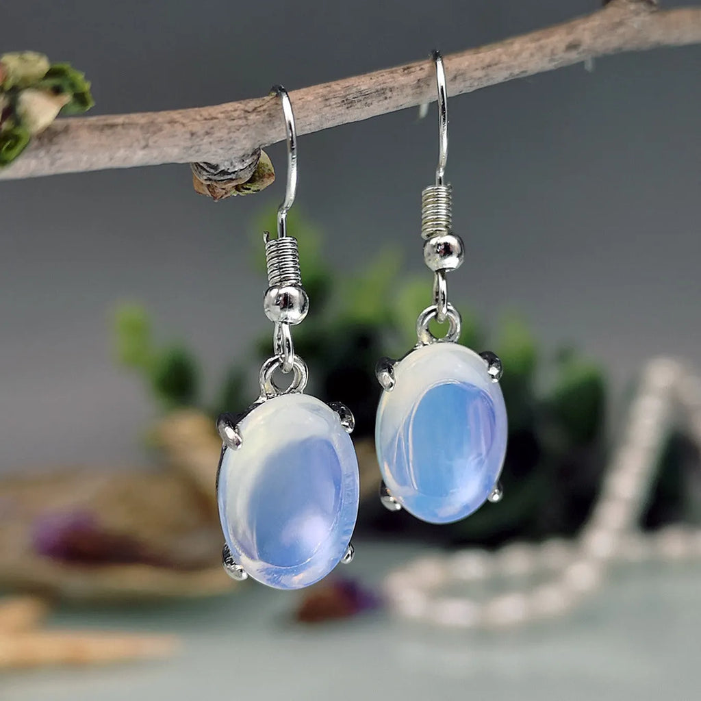 A pair of retro-style opal drop earrings in moonlight white with a cross detail and ellipse shapes.