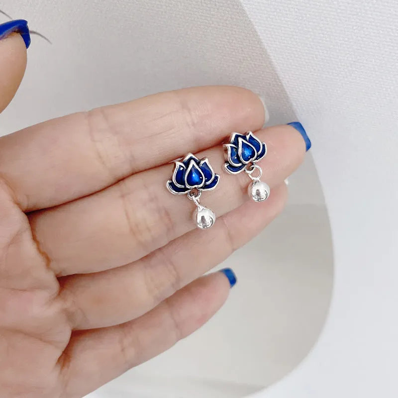 Close-up of blue lotus seedpod and tassel drop earrings in silver tone alloy on a white background.