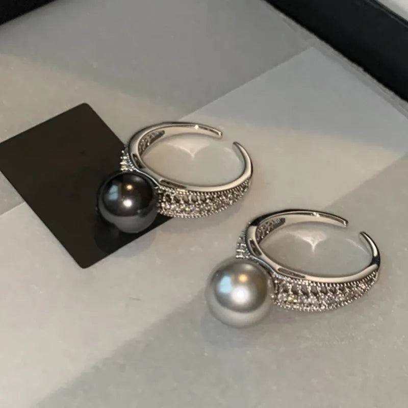 Geometric adjustable open ring in black pearl colour on a copper band, shown on a woman's index finger.