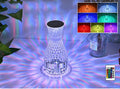 Transparent vase-shaped crystal LED table lamp with multi-colour lights on a wooden table.