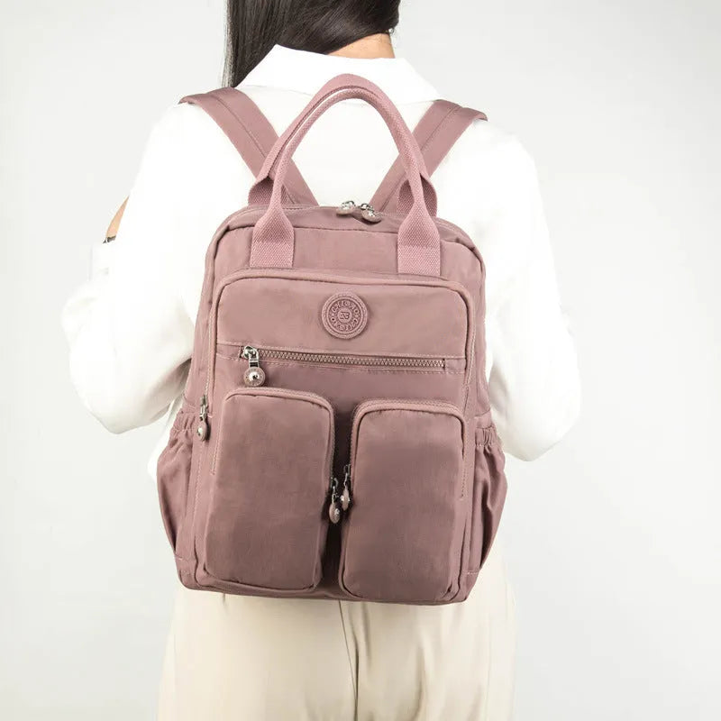 Waterproof nylon women's backpack in grey showing front pockets and internal laptop compartment.