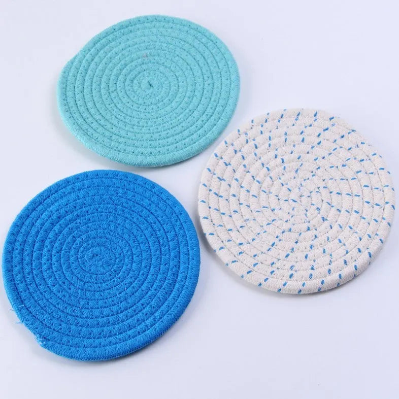 Set of three round cotton cord coasters in blue colour, 18cm diameter, on a table.