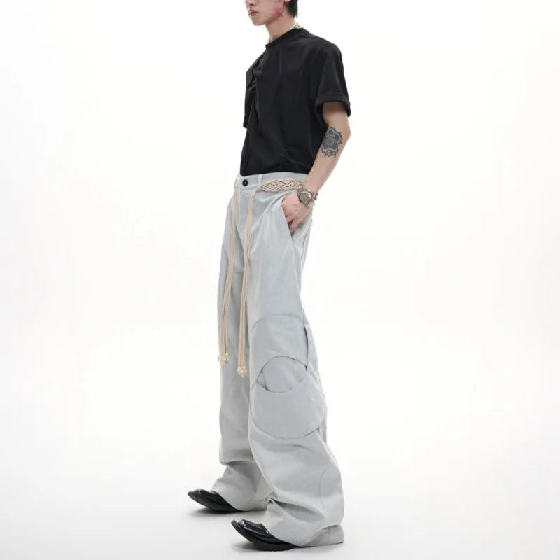 Man wearing dark grey straight-leg cotton trousers with a tassel detail and loose fit.