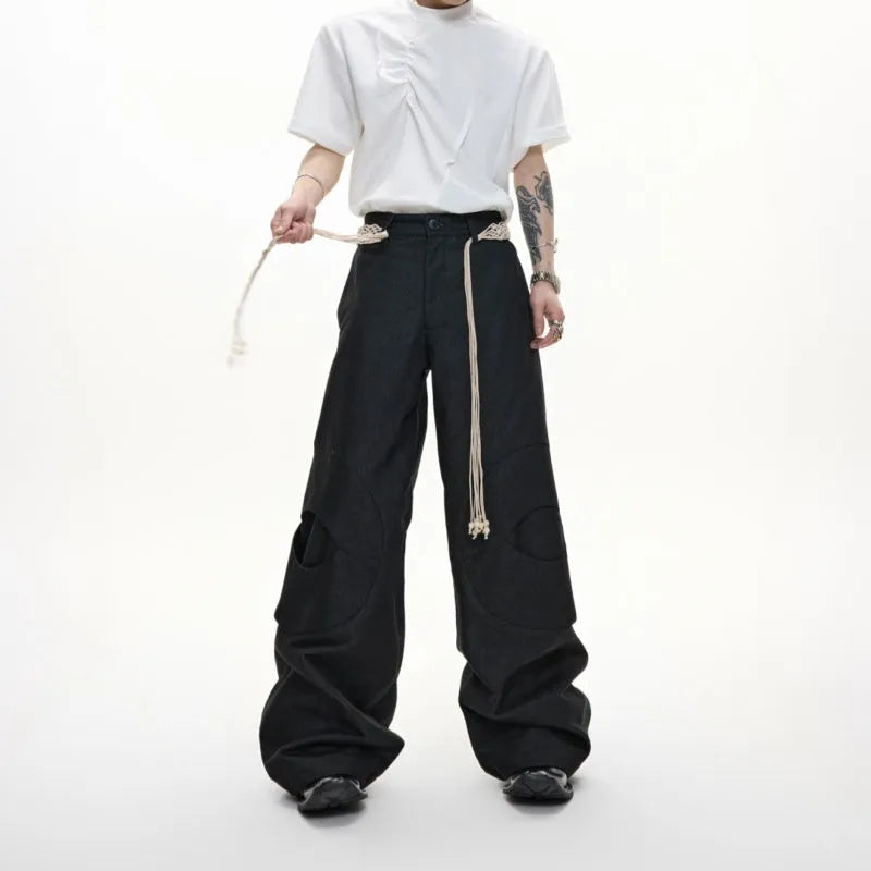 Man wearing dark grey straight-leg cotton trousers with a tassel detail and loose fit.