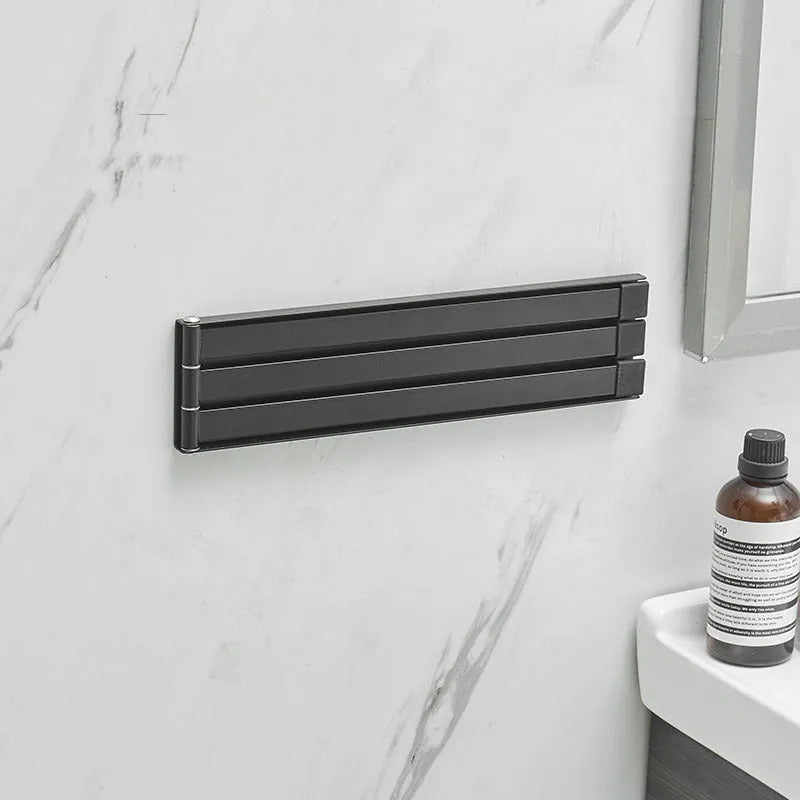 Black folding towel bar mounted on a bathroom wall with adhesive, shown in extended and folded positions.