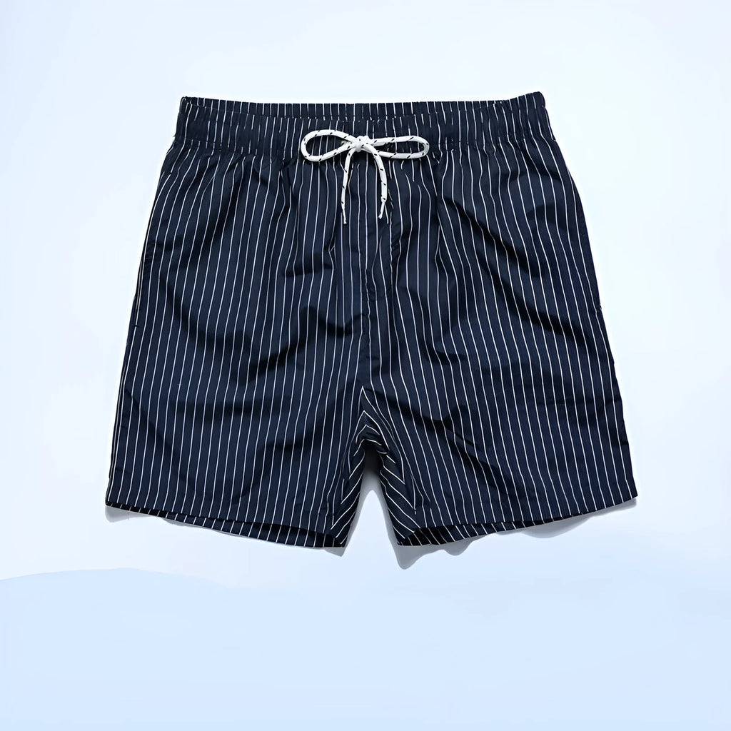 Man wearing grey striped polyester beach shorts with a straight leg opening, on a beach.