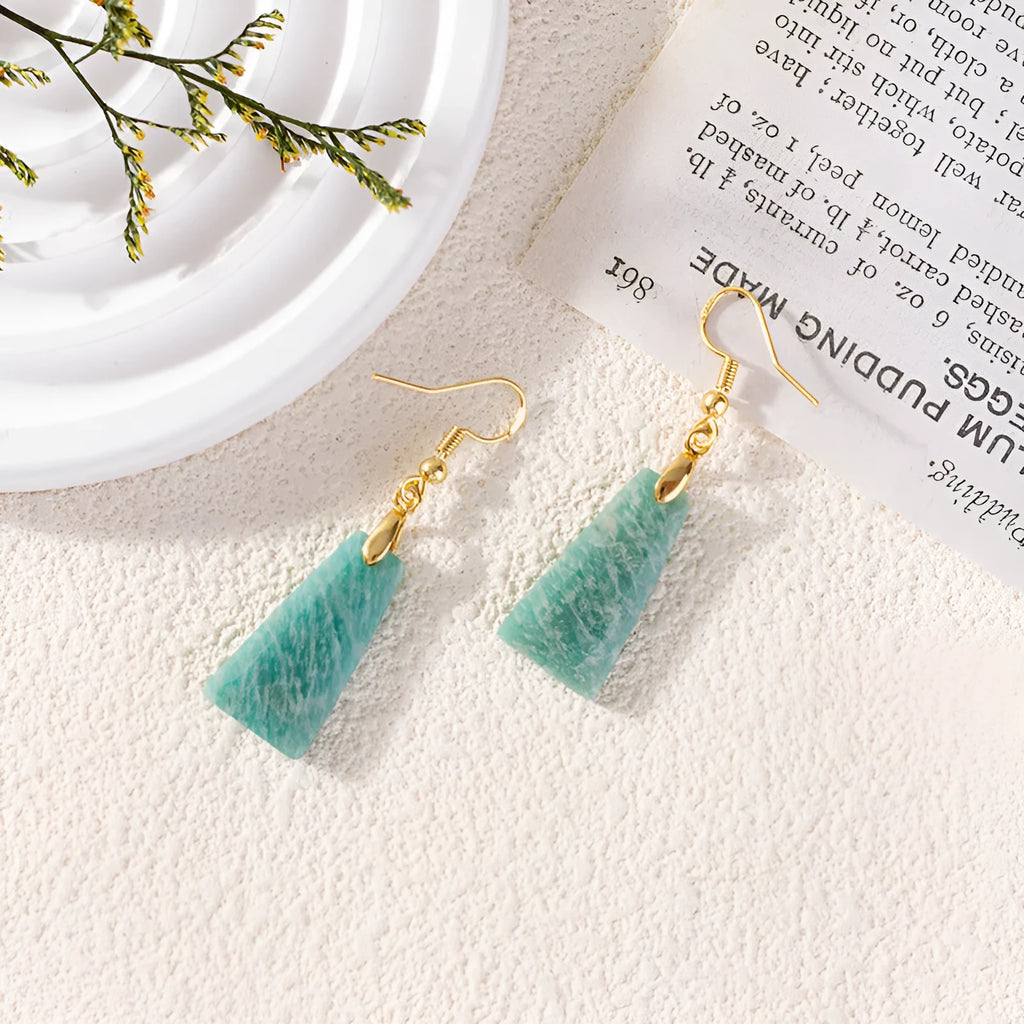 A pair of trapezoid-shaped earrings with a rough green amazonite stone set in a geometric gold or silver metal frame.