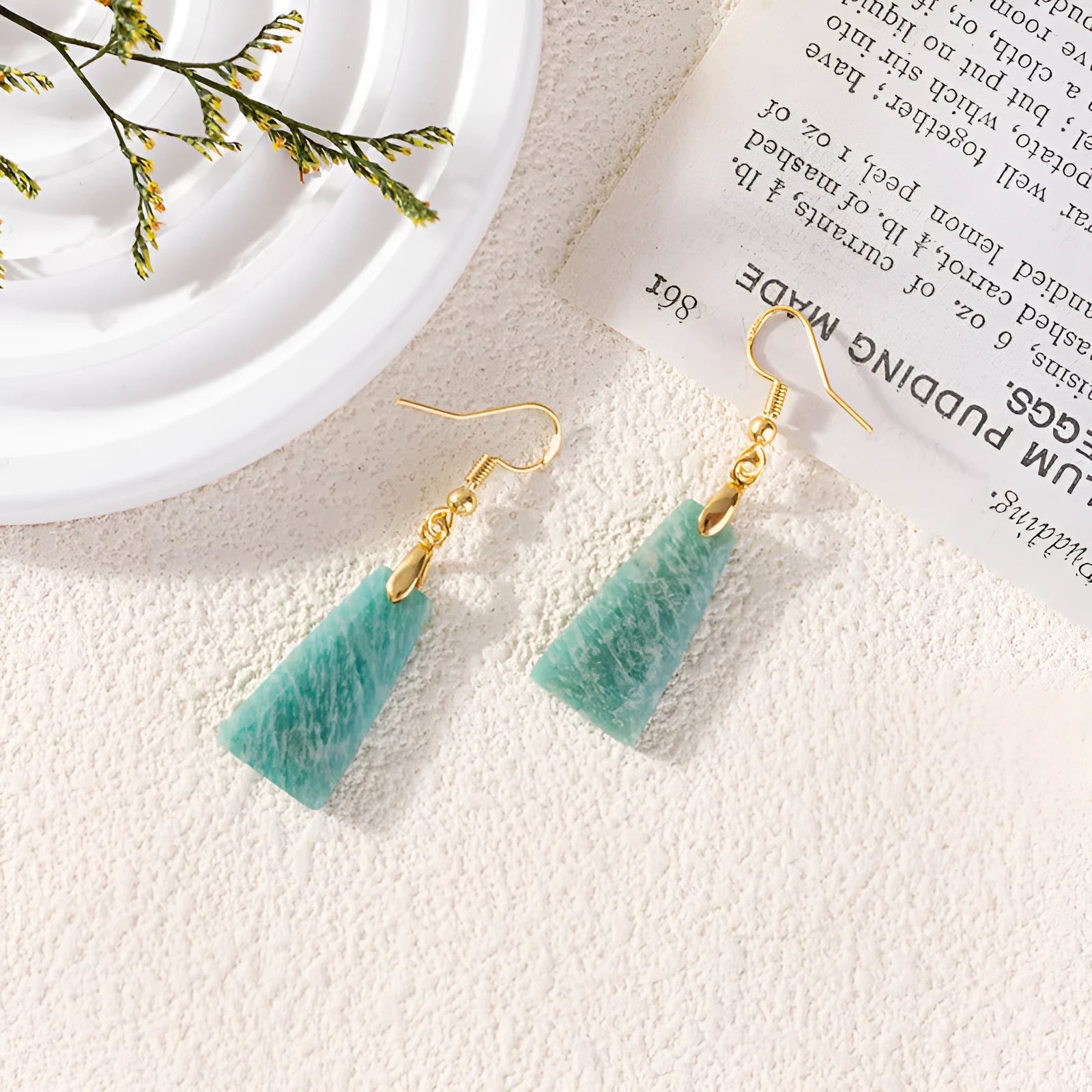 A pair of trapezoid-shaped earrings with a rough green amazonite stone set in a geometric gold or silver metal frame.