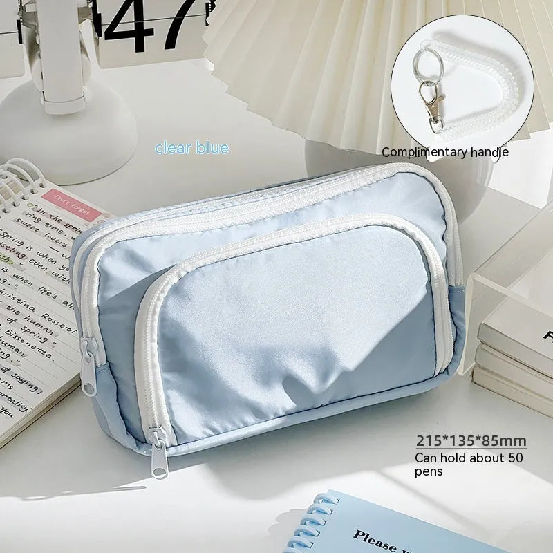 Double layer zippered pencil case in blue with a gift handle, shown next to pens and pencils.