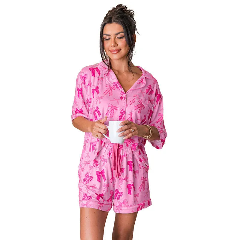 Women's pink polyester pajama set with bow print, featuring a top and trousers.