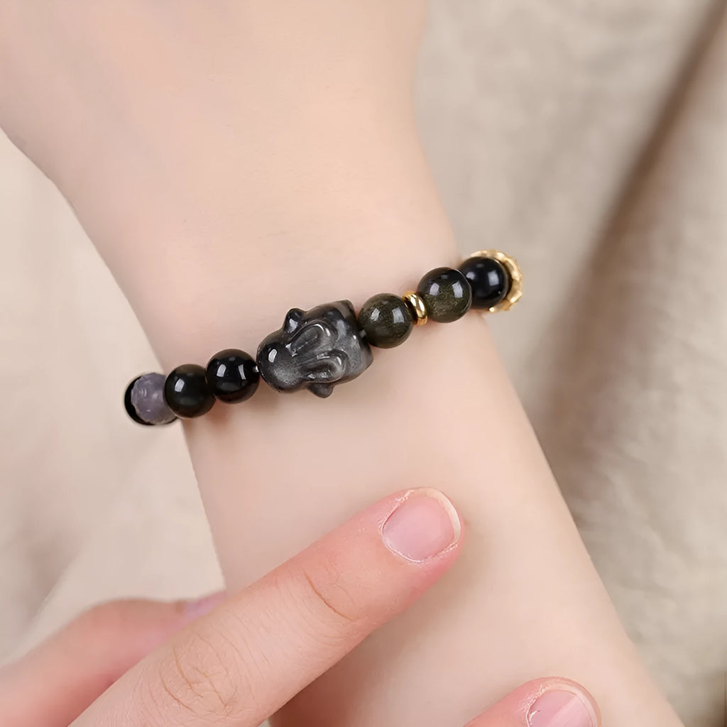 Handmade lying rabbit obsidian bracelet with grey agate beads and brass details on a wrist.