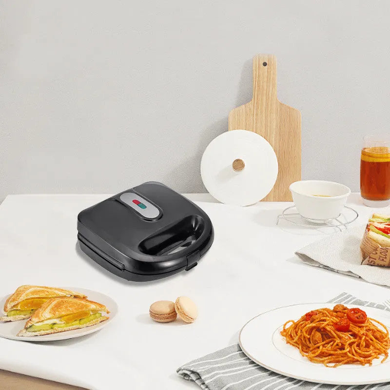 Black electric sandwich pan with stainless steel lid on a kitchen countertop.