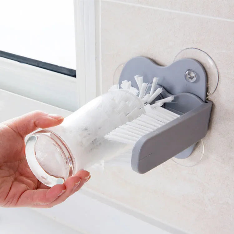 Grey 2 in 1 cup scrubber with double-sided bristles and three suction cups on the base for cleaning glassware.