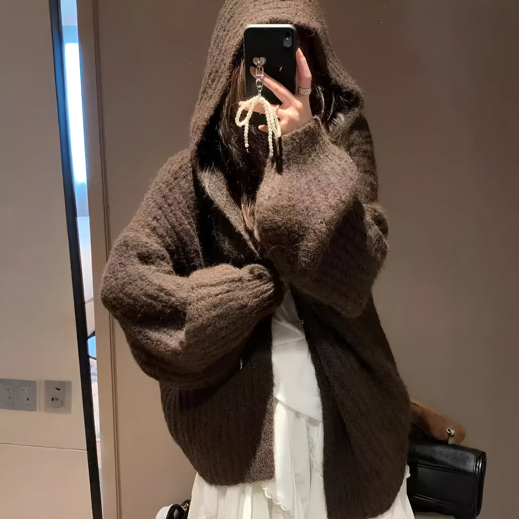 Women's retro-style thick knitted hooded cardigan in dark grey, shown open over a top.