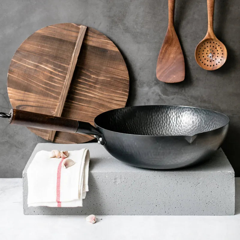 Black traditional cast iron wok pan with wooden handle and glass lid on induction hob