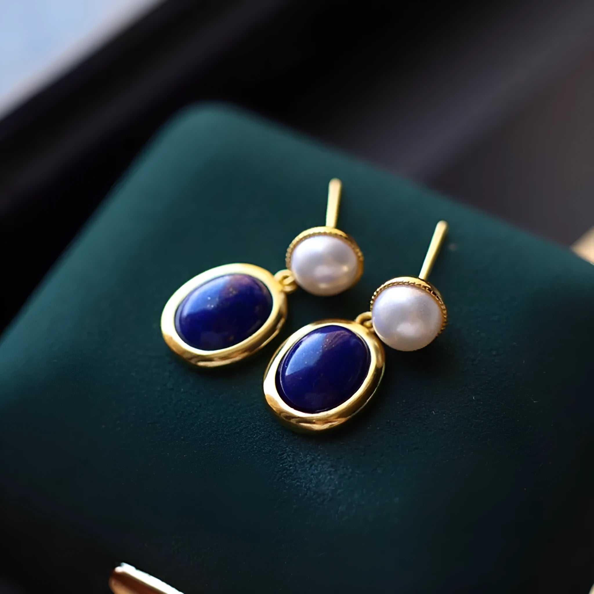 A pair of simple sterling silver earrings featuring blue lapis lazuli pearls and auspicious pattern detailing.