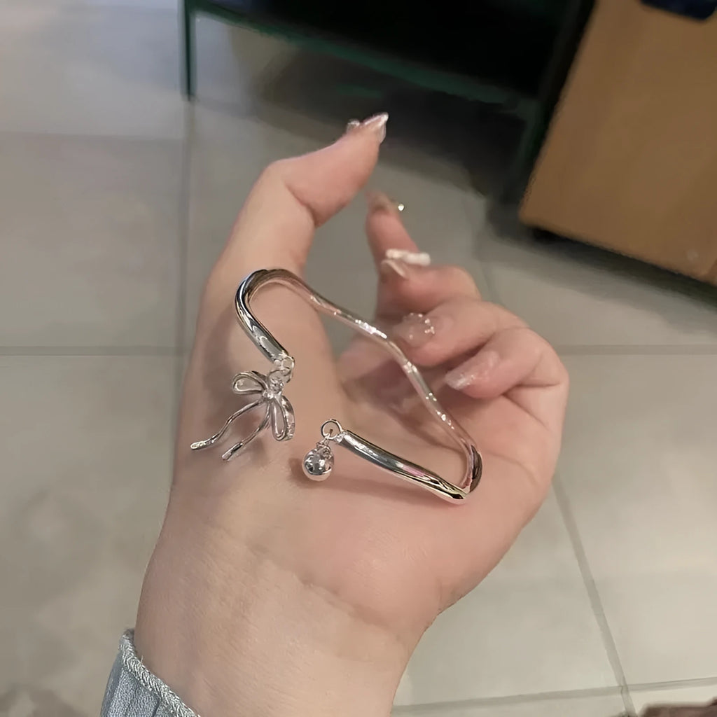 Silver adjustable bracelet with a bow charm and small bell on a zinc alloy band.