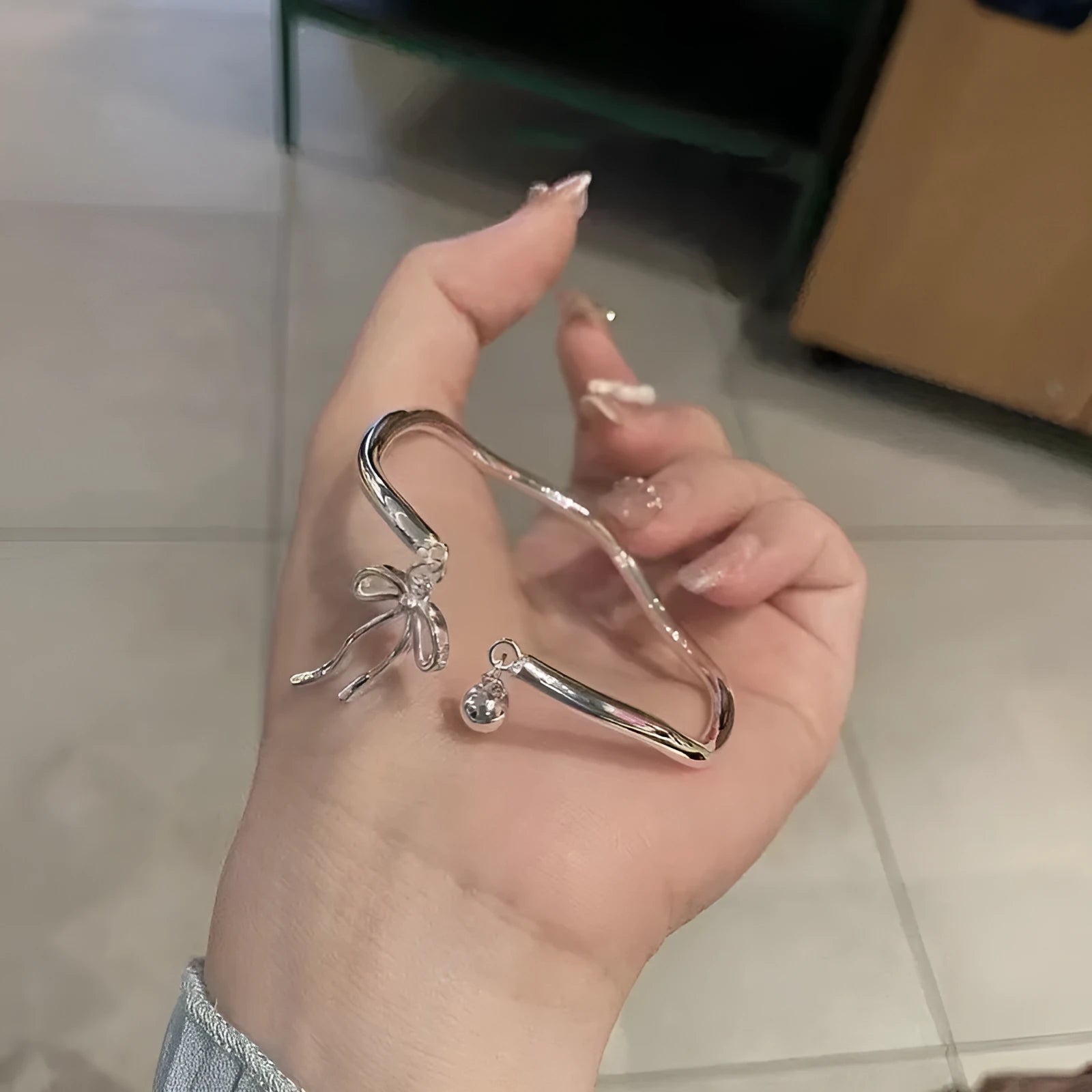Silver adjustable bracelet with a bow charm and small bell on a zinc alloy band.