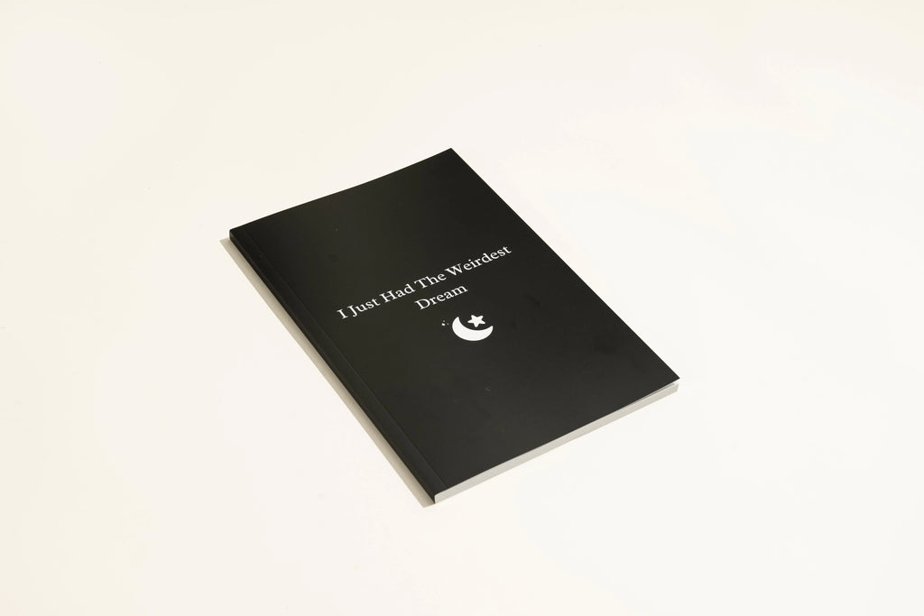 Black hardcover A5 dot grid Dream Journal notebook open on a dot grid cream paper page.