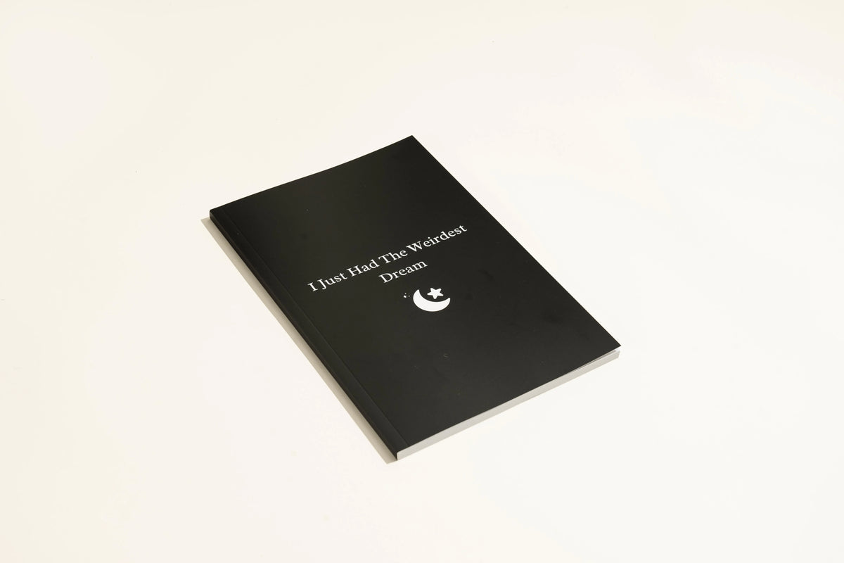 Black hardcover A5 dot grid Dream Journal notebook open on a dot grid cream paper page.
