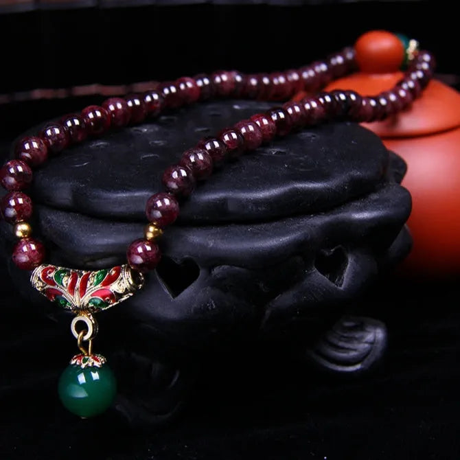 Red garnet bracelet with 7mm beads and a golden toad charm on wrist.