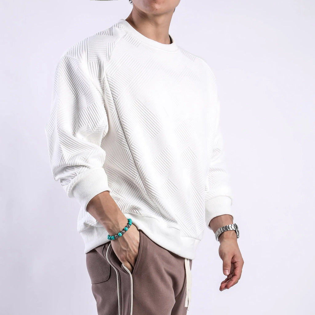 Man wearing a loose-fitting, long-sleeved army green pullover sweater with a textured twill jacquard pattern.