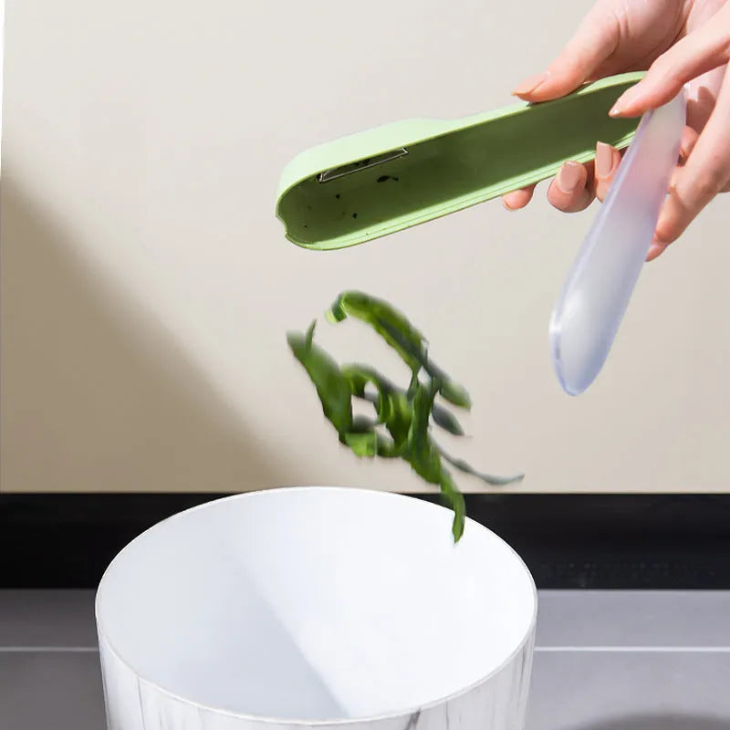 Dark green vegetable peeler with a storage tube and stainless steel blade on a kitchen worktop.