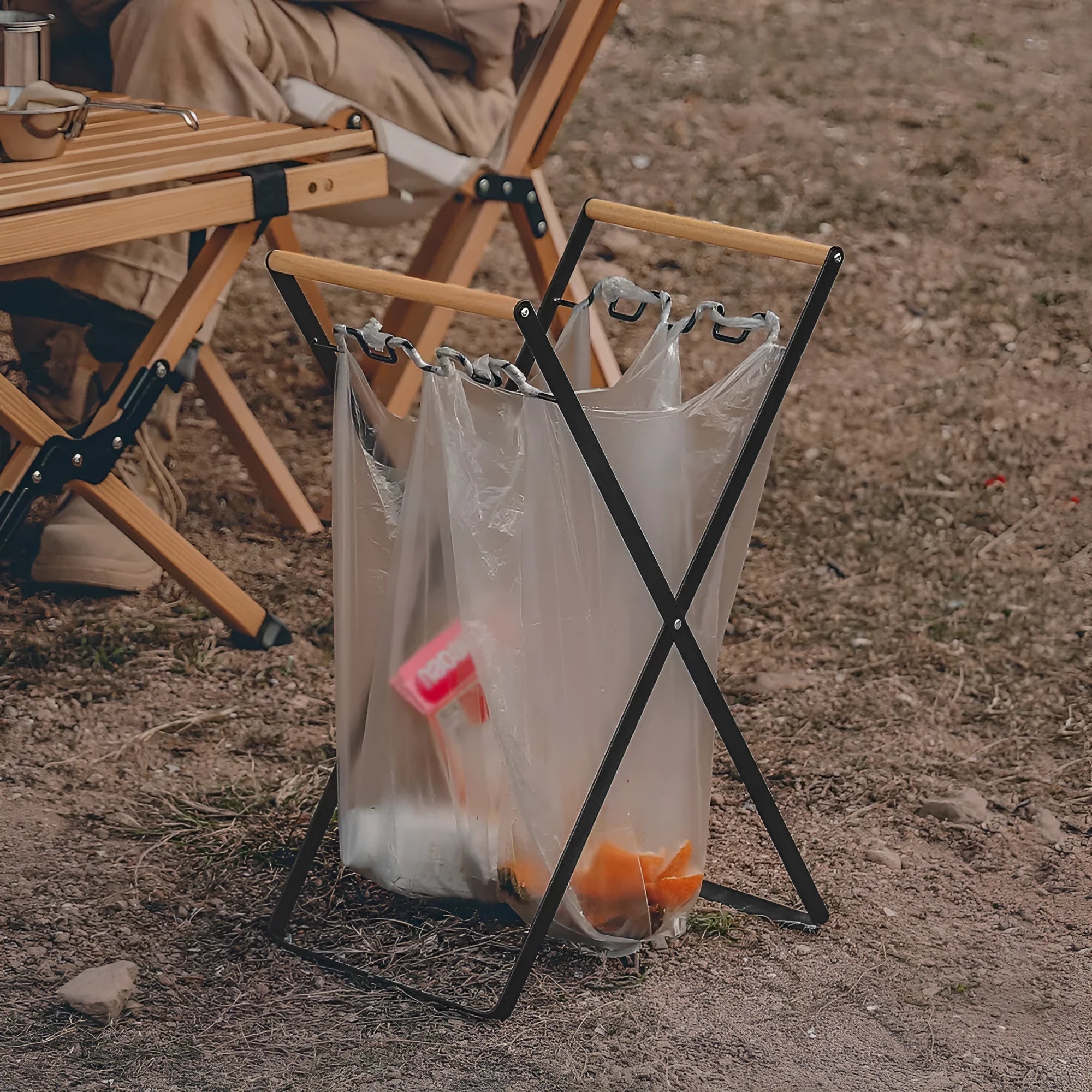 Black foldable outdoor iron trash rack with wooden handle holding a white bin bag.