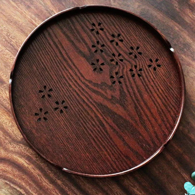 Wooden circular serving platter with 12 round compartments and a central carved cherry blossom (sakura) design.