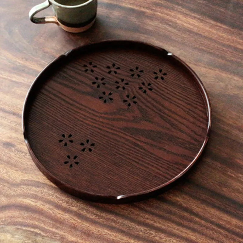 Wooden circular serving platter with 12 round compartments and a central carved cherry blossom (sakura) design.