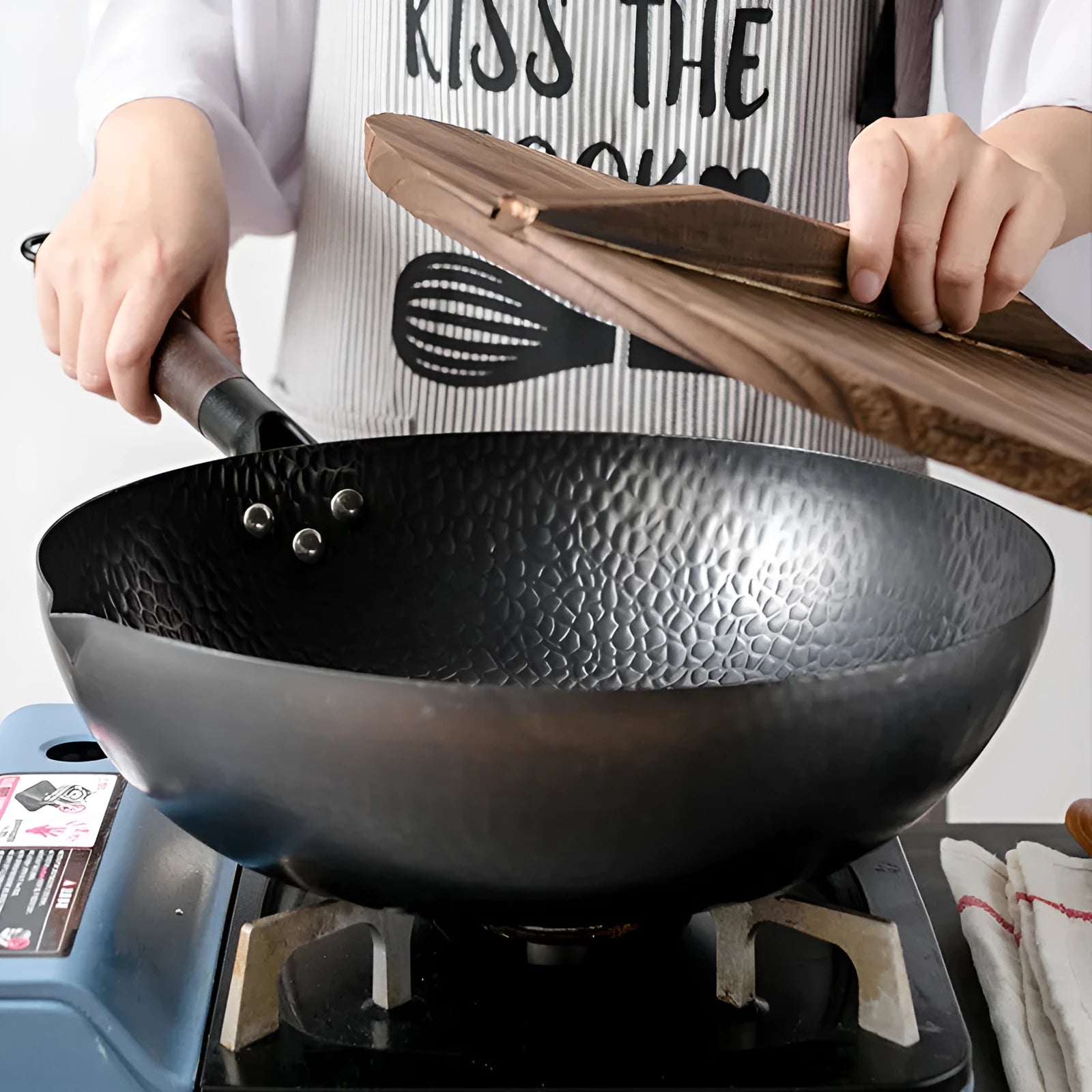 Black traditional cast iron wok pan with wooden handle and glass lid on induction hob
