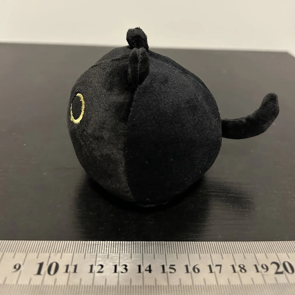Black fluffy cat plush toy stuffed animal on a sofa, used as a soft cushion.
