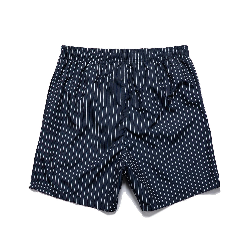 Man wearing grey striped polyester beach shorts with a straight leg opening, on a beach.