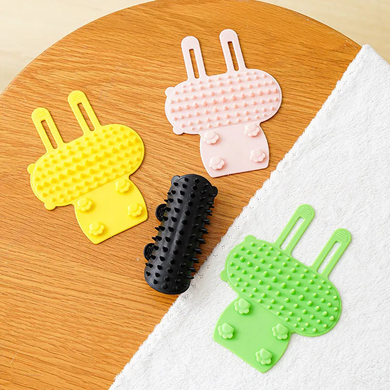 Adjustable silicone cat scratching grooming brush in black, mounted on a table leg.