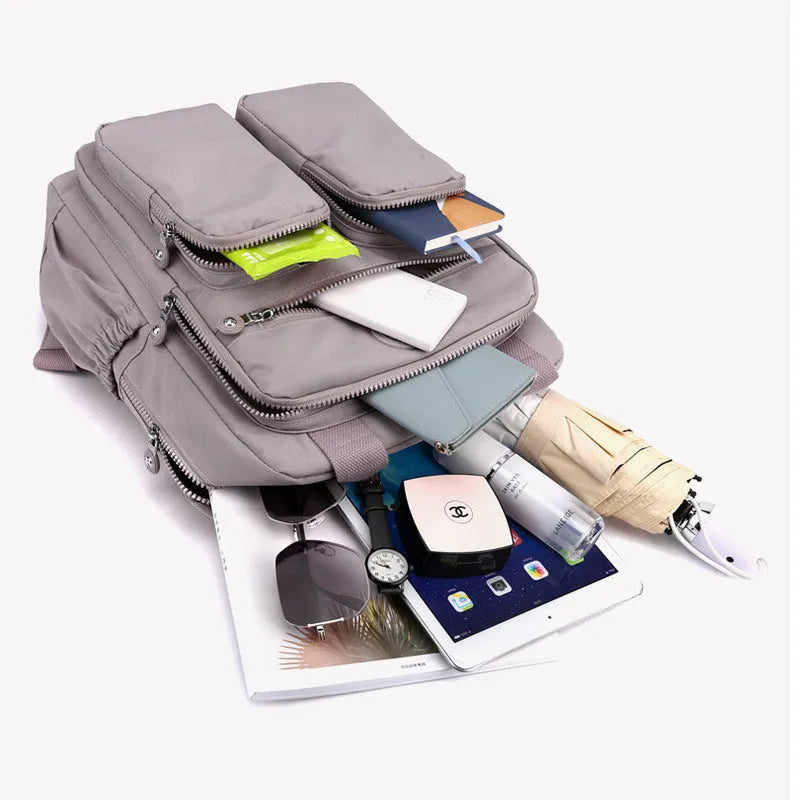 Waterproof nylon women's backpack in grey showing front pockets and internal laptop compartment.