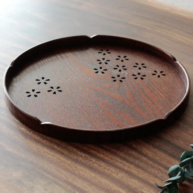 Wooden circular serving platter with 12 round compartments and a central carved cherry blossom (sakura) design.