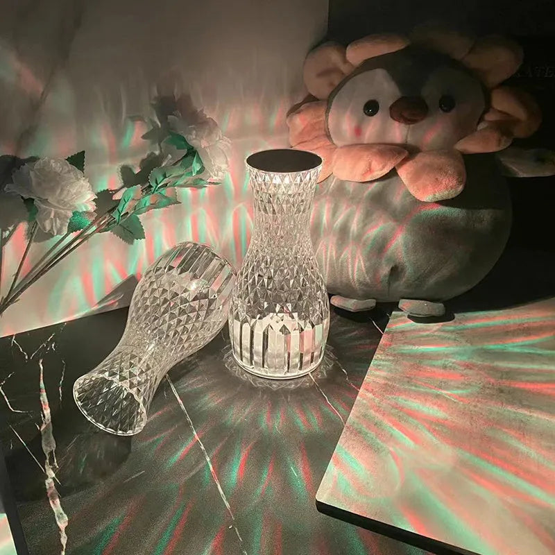 Transparent vase-shaped crystal LED table lamp with multi-colour lights on a wooden table.