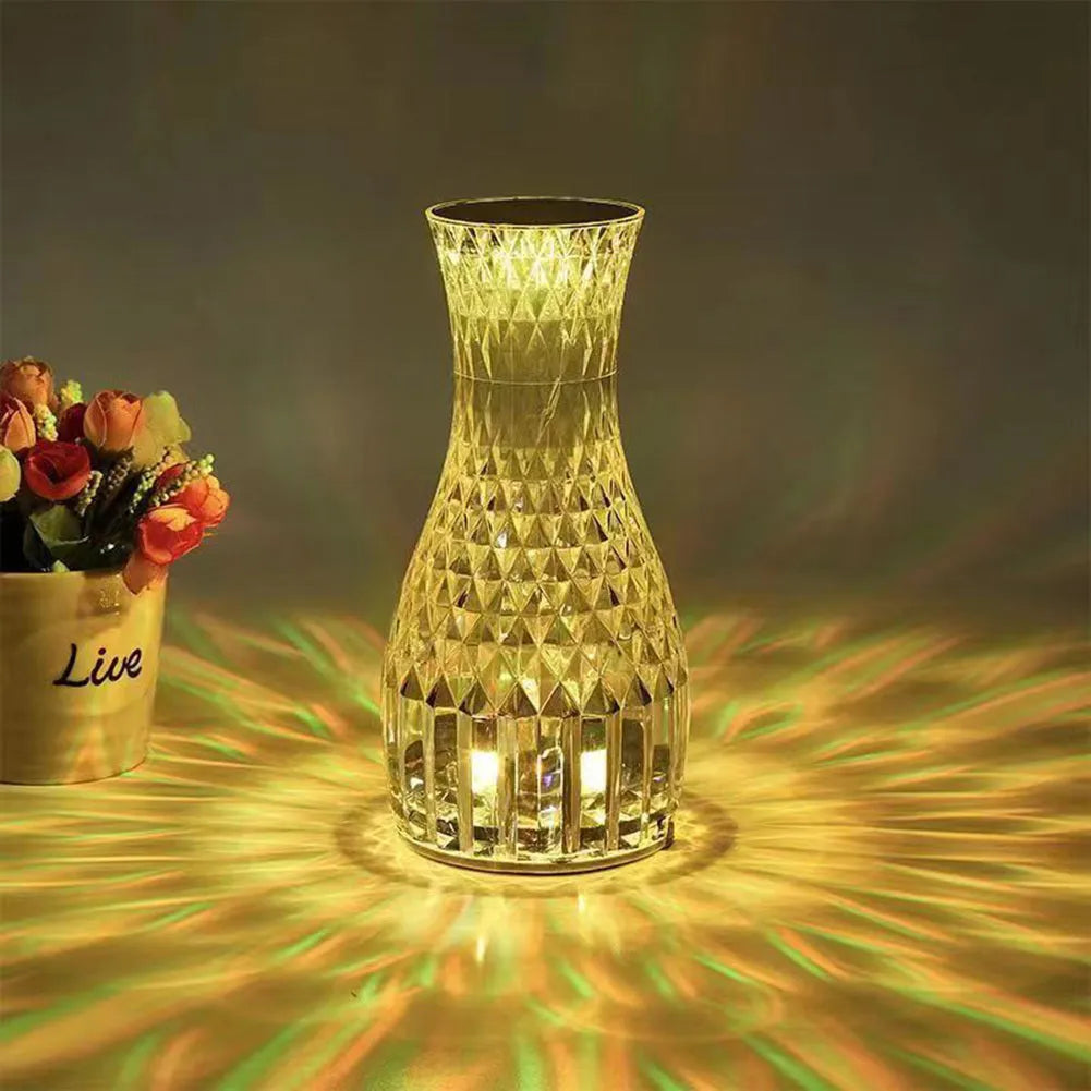Transparent vase-shaped crystal LED table lamp with multi-colour lights on a wooden table.