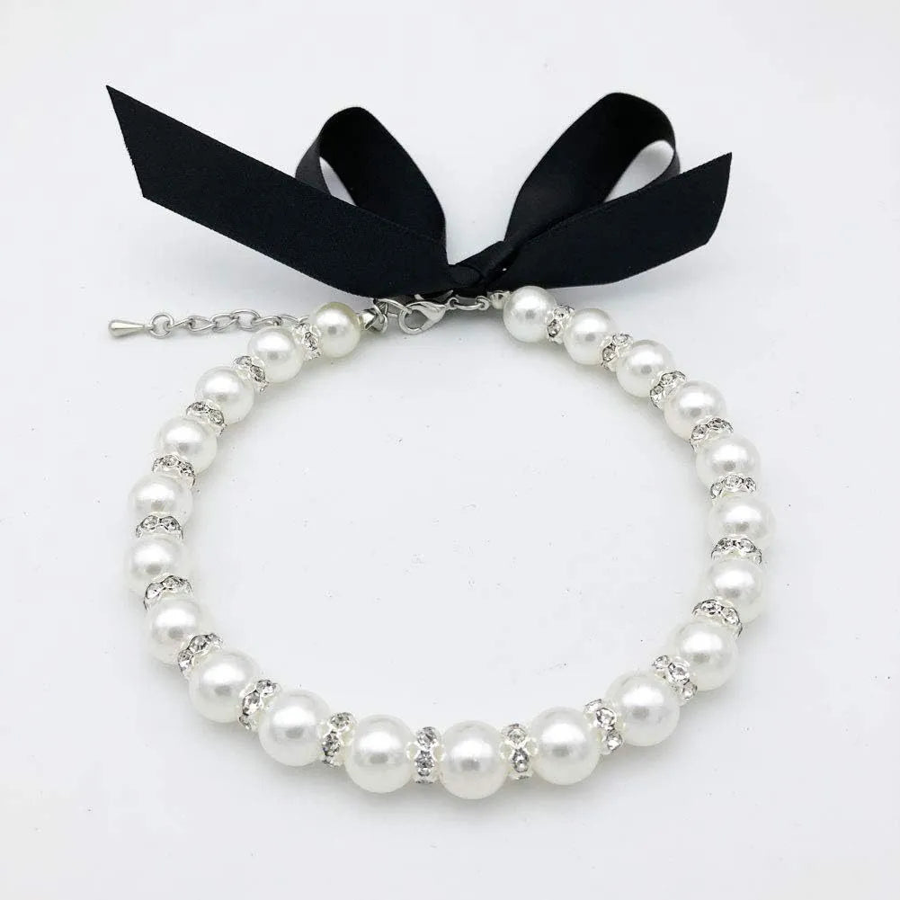 Small dog wearing an adjustable blue pearl and rhinestone necklace with a ribbon bow on a soft ribbon.