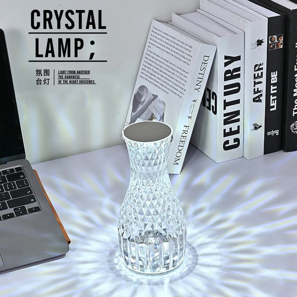 Transparent vase-shaped crystal LED table lamp with multi-colour lights on a wooden table.