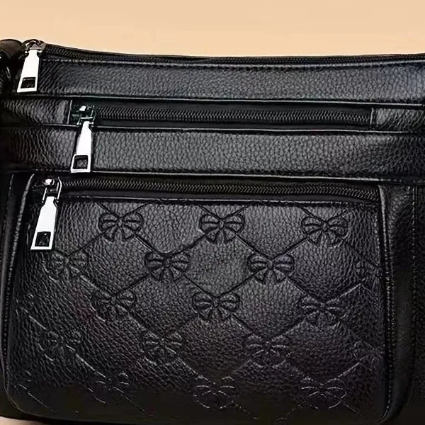 Black women's crossbody bag with embossed butterfly pattern showing phone pocket and external slit